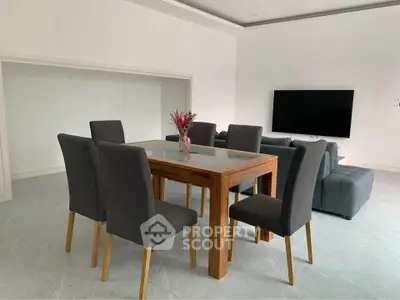 Modern dining area with sleek glass table and stylish gray chairs in a spacious living room.
