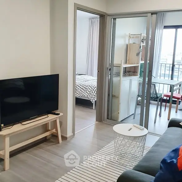 Modern living room with TV, cozy seating, and view into bedroom and balcony.