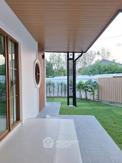 Modern home exterior with stylish patio and lush green lawn, featuring elegant wood accents and large windows.