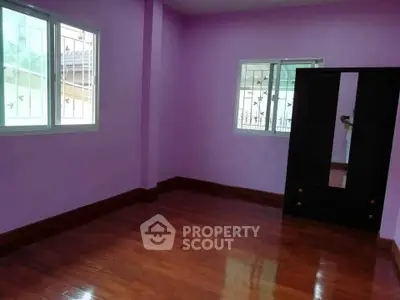 Spacious empty bedroom with wooden floors and purple walls, featuring a window and wardrobe.