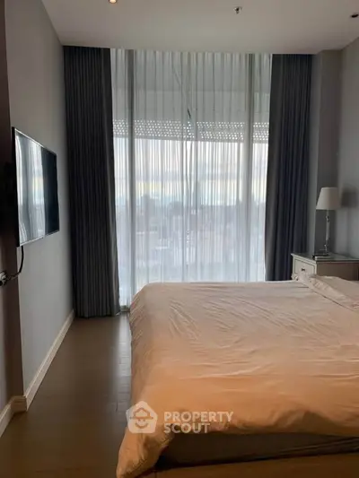 Modern bedroom with large window and flat-screen TV, featuring elegant curtains and a cozy bed.