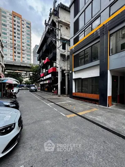 Urban street view with modern buildings and parked cars, showcasing city living environment.