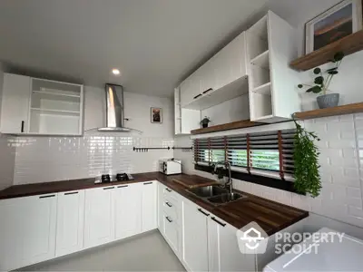 Modern kitchen with white cabinetry and wooden countertops, featuring a gas stove and stylish decor.