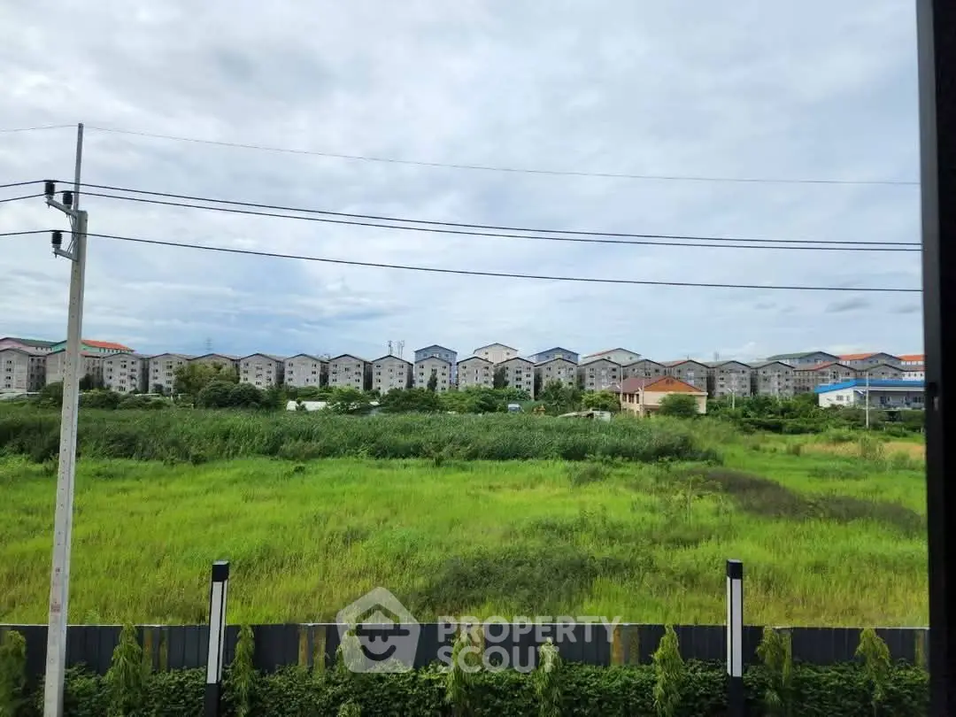 Scenic view of residential buildings across lush green field under cloudy sky.