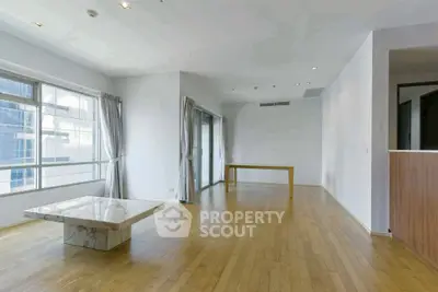 Spacious modern living room with wooden floors and large windows in high-rise apartment.