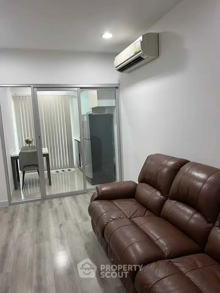 Modern living room with leather sofa and air conditioning, adjacent to a sleek kitchen with sliding glass doors.