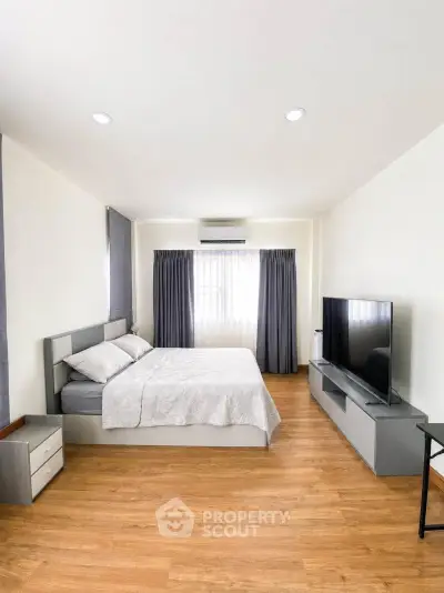 Spacious modern bedroom with wooden flooring and large TV unit