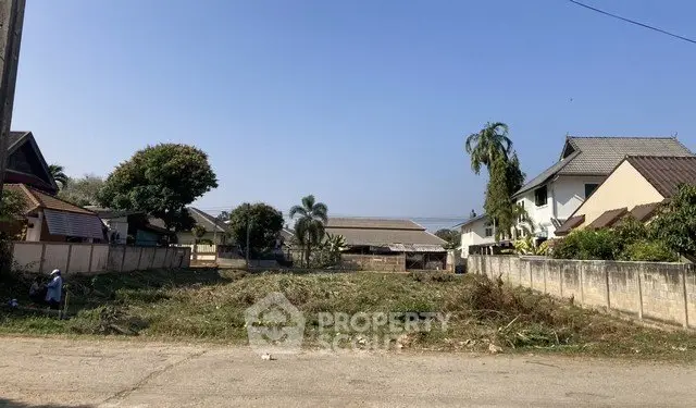 Vacant land plot in a residential neighborhood with clear blue sky, ideal for building a dream home.