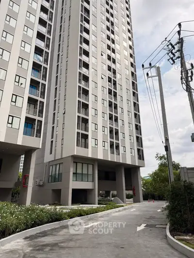 Modern high-rise apartment building with landscaped entrance and clear sky.