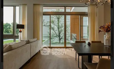 Elegant living room with large windows and modern dining area, offering a serene view of greenery.