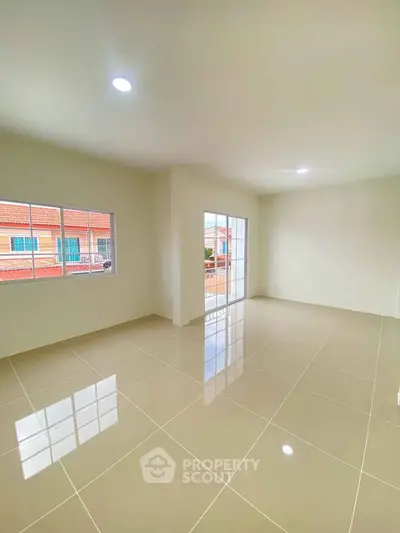 Spacious empty room with glossy tiled floors and large windows offering natural light.