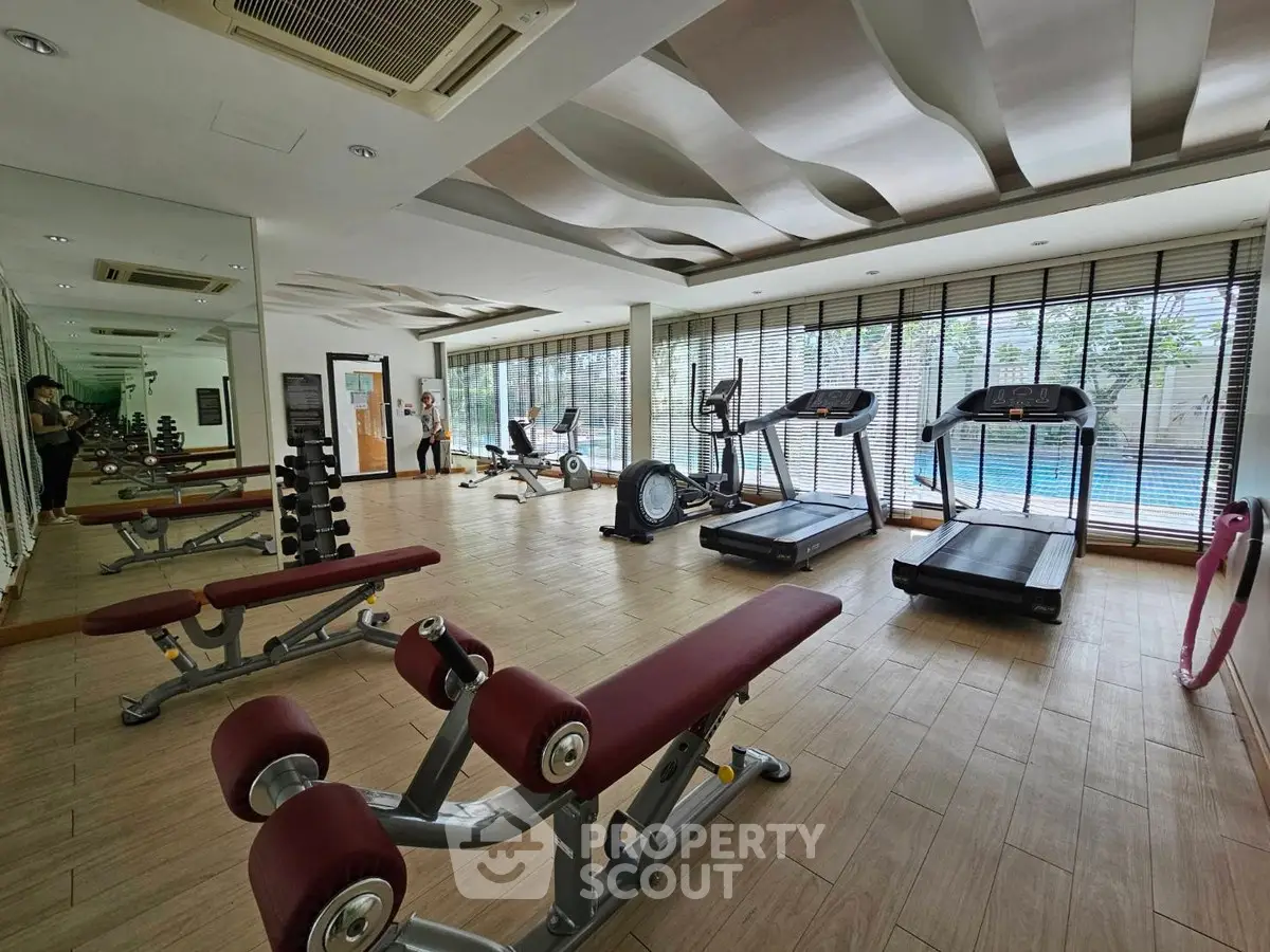 Spacious gym with modern equipment and pool view in luxury real estate property.