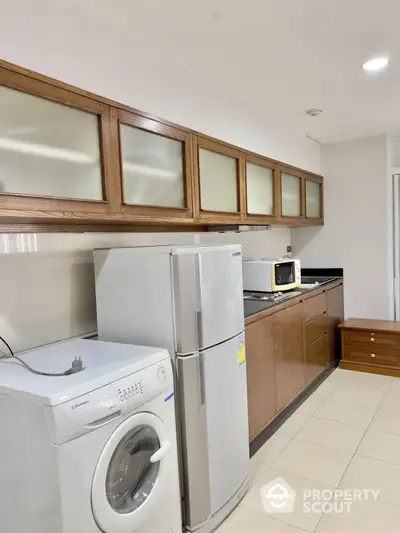 Modern kitchen with wooden cabinets, washing machine, and refrigerator in a sleek design.