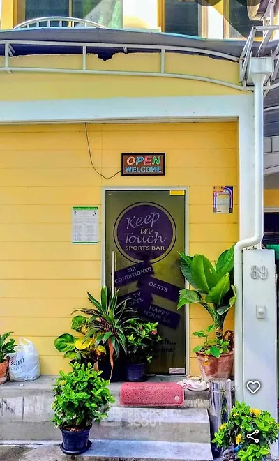 Charming yellow building entrance with lush plants and inviting signage, perfect for a cozy sports bar experience.