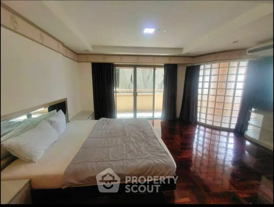 Spacious bedroom with elegant wooden flooring and large windows for natural light.