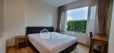 Cozy bedroom with large window and garden view, featuring wooden furniture and a comfortable bed.