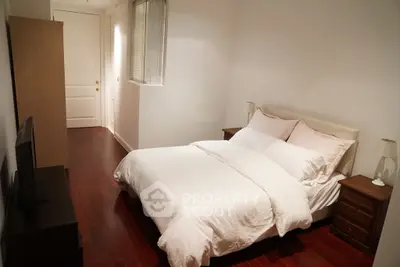 Cozy bedroom with wooden flooring and elegant white bedding in modern apartment.