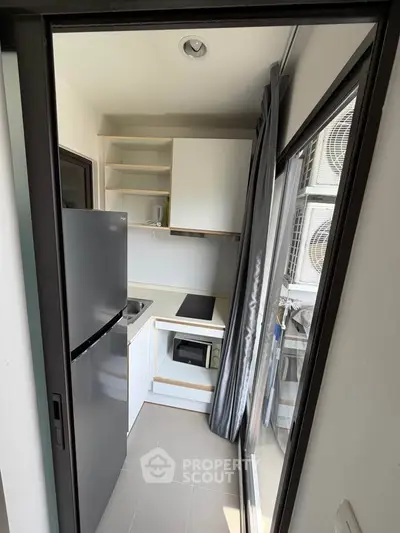 Compact modern kitchen with sleek appliances and balcony access in urban apartment.