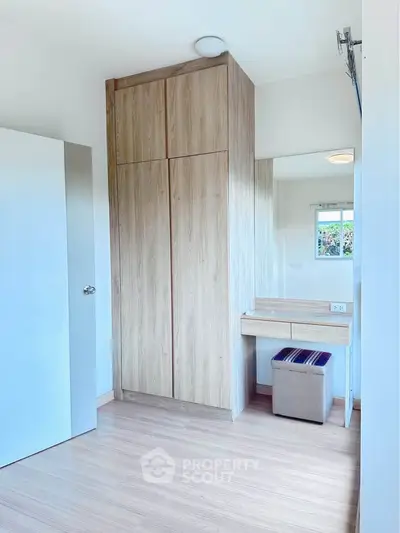 Bright bedroom with wooden wardrobe and vanity, featuring natural light and modern design.