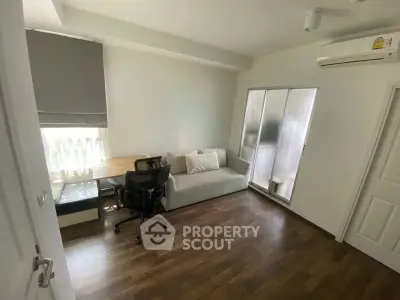 Modern study room with wooden flooring, desk, chair, and sofa, featuring natural light and air conditioning.