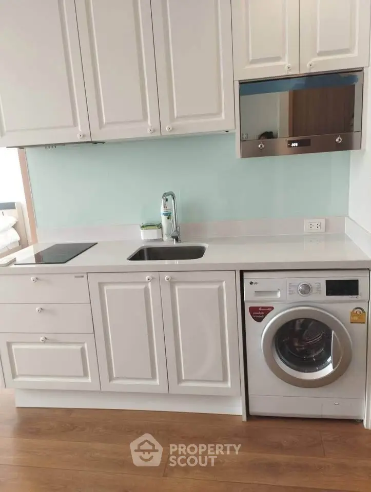 Modern kitchen with white cabinetry, washing machine, and sleek appliances in a compact layout.
