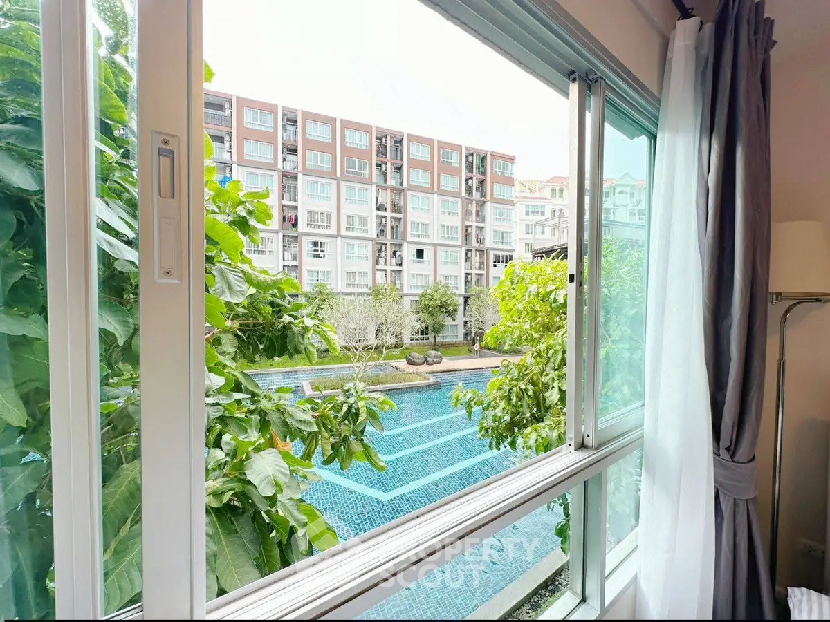 Spacious apartment with stunning pool view through large windows, offering serene and lush greenery.