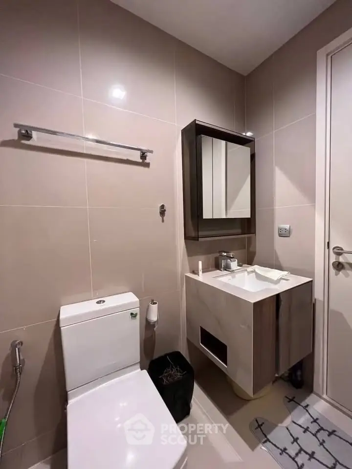 Modern bathroom with sleek fixtures and neutral tiles, featuring a compact vanity and toilet.