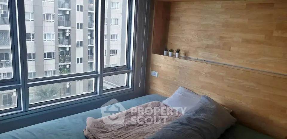 Cozy bedroom with large window offering urban view and wooden accent wall.