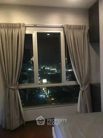 Cozy bedroom with stunning city night view from large window, perfect for urban living.