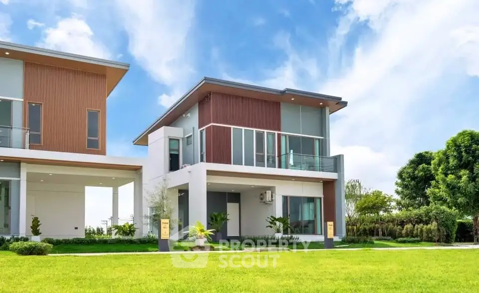 Modern two-story house with large windows and lush green lawn under a clear blue sky.
