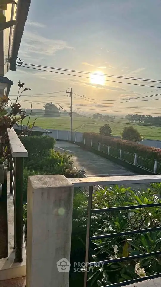 Stunning sunrise view from a balcony overlooking lush greenery and open fields.