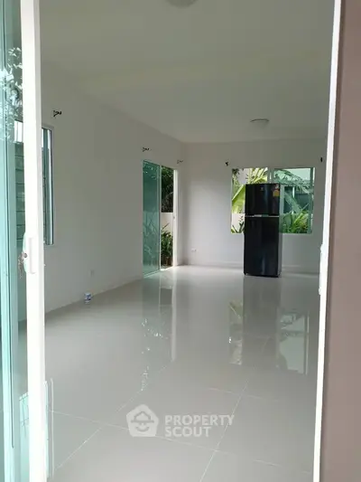 Spacious modern living room with glossy tiled floors and large windows, featuring a sleek black refrigerator.