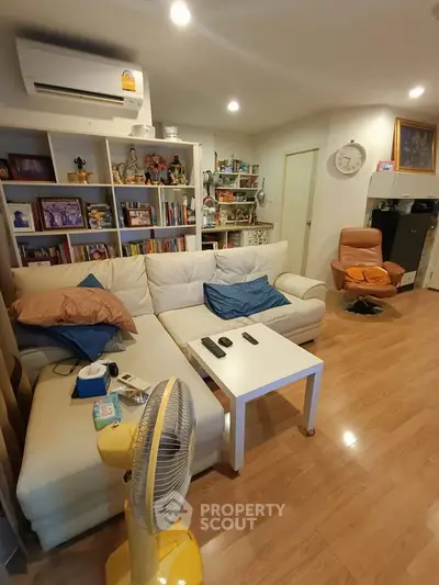 Cozy living room with modern decor, featuring a white sectional sofa, wooden flooring, and a stylish bookshelf.