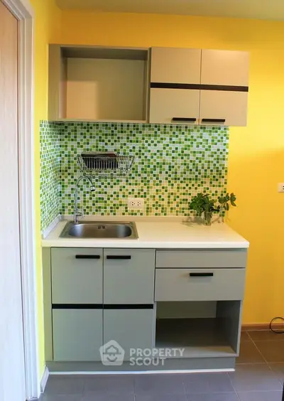 Modern compact kitchen with vibrant yellow walls and green mosaic backsplash.