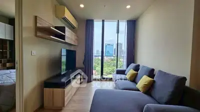 Modern living room with large window and city view, featuring cozy gray sofas and wooden TV unit.