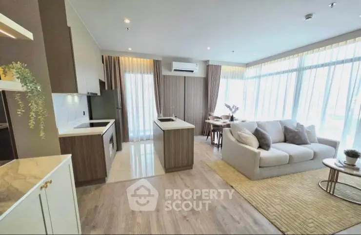 Modern open-layout living room with kitchen, featuring stylish decor and large windows for natural light.