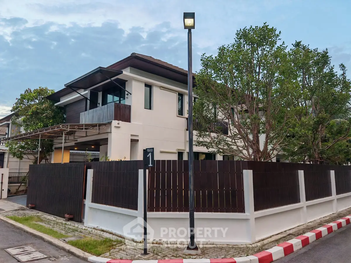 Modern two-story house with fenced yard and street view, featuring contemporary architecture and lush greenery.