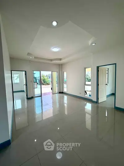 Spacious modern living room with large windows and glossy tiled floors, offering abundant natural light.