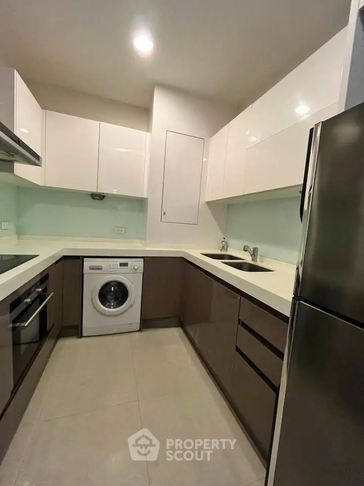 Modern kitchen with sleek cabinets, washing machine, and stainless steel appliances.