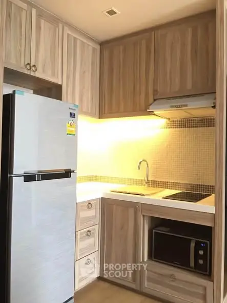 Modern kitchen with wooden cabinets, built-in microwave, and sleek refrigerator in a cozy apartment.