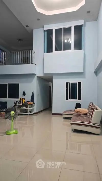 Spacious living room with high ceiling and modern design, featuring a cozy seating area and sleek tiled flooring.