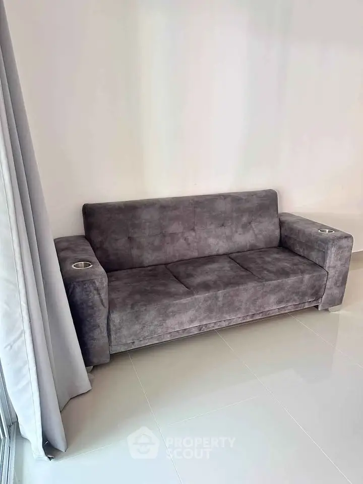 Modern gray sofa in a minimalist living room with sleek tile flooring and neutral curtains.