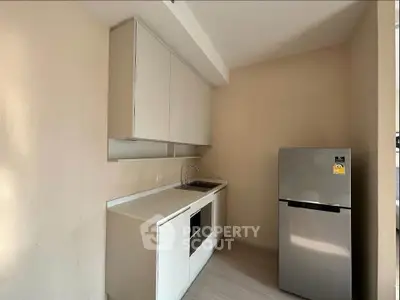 Modern compact kitchen with sleek cabinetry and stainless steel fridge in a cozy apartment.