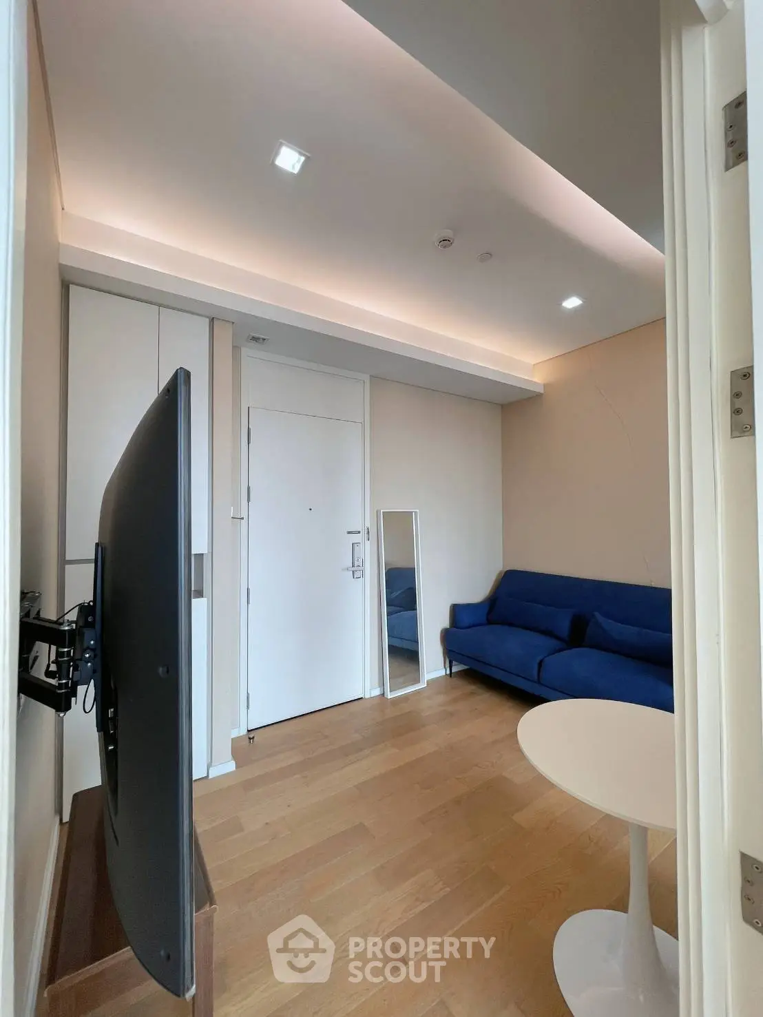 Modern living room with sleek design, featuring a blue sofa, wall-mounted TV, and stylish lighting.