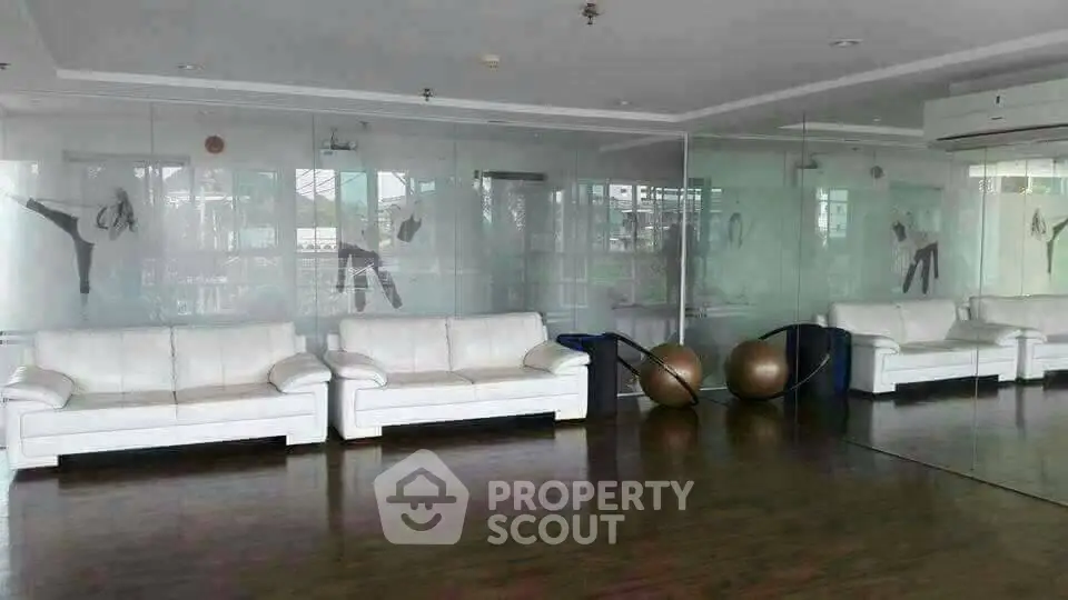 Spacious gym with mirrored walls and white sofas, perfect for fitness enthusiasts.