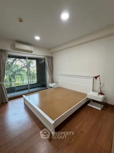 Spacious bedroom with wooden flooring and balcony view, featuring modern minimalist design.