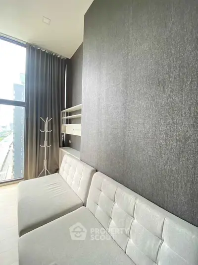 Modern living room with sleek gray sofa and large window offering city view