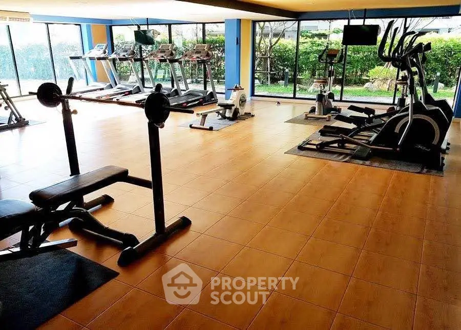 Spacious gym with modern equipment and large windows offering garden views, perfect for fitness enthusiasts.