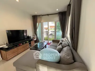 Modern living room with large sofa and entertainment center, featuring natural light from glass doors.