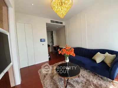 Elegant living room with plush blue sofa, chic chandelier, and cozy rug in modern apartment.